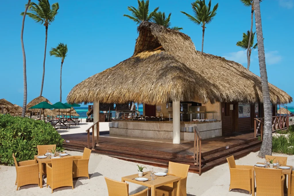 Barefoot Grill beachside restaurant at Secrets Royal Beach Punta Cana with a thatched-roof palapa, outdoor seating on the sand, and ocean views.