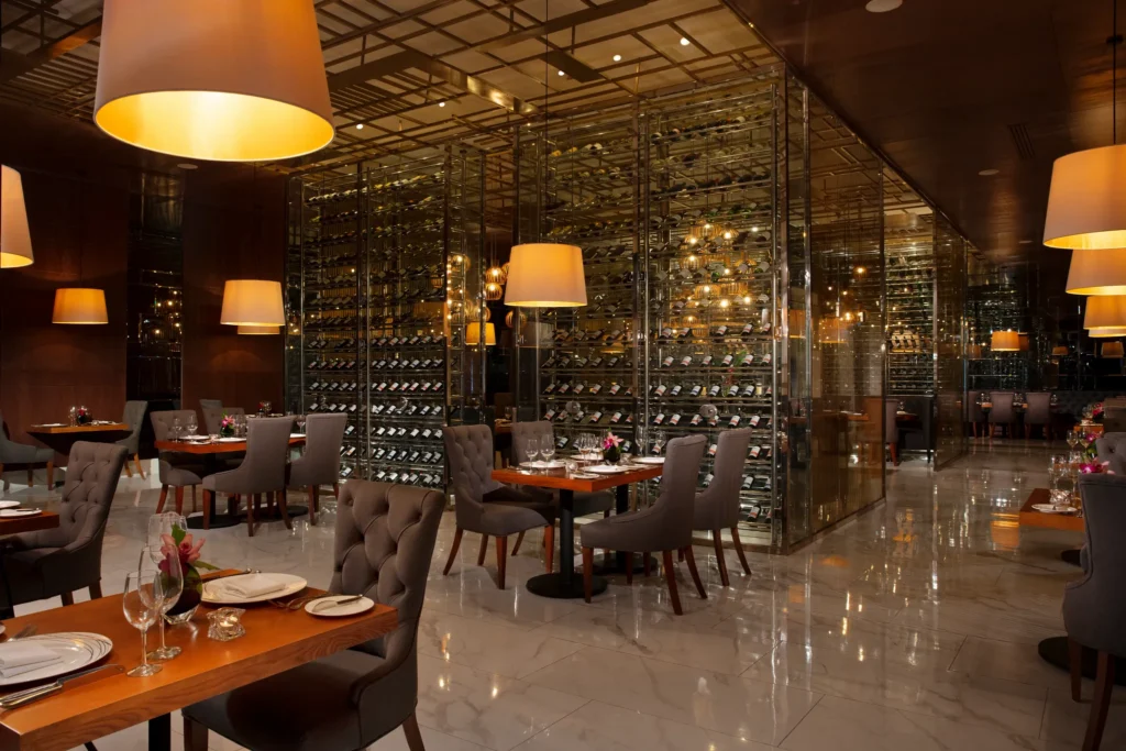Bordeaux French Restaurant at Secrets Royal Beach Punta Cana featuring elegant dining tables and a glass-enclosed wine cellar display.