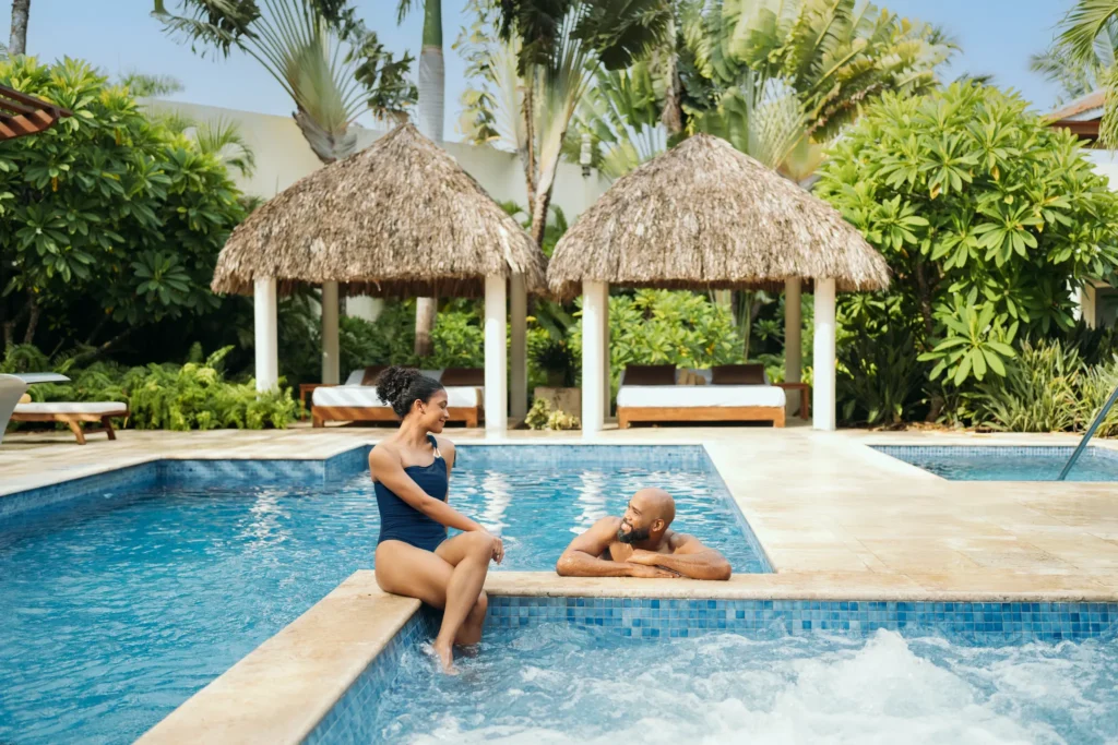 Couple relaxing together in the hydrotherapy spa pool surrounded by tropical cabanas at Secrets Royal Beach Punta Cana.