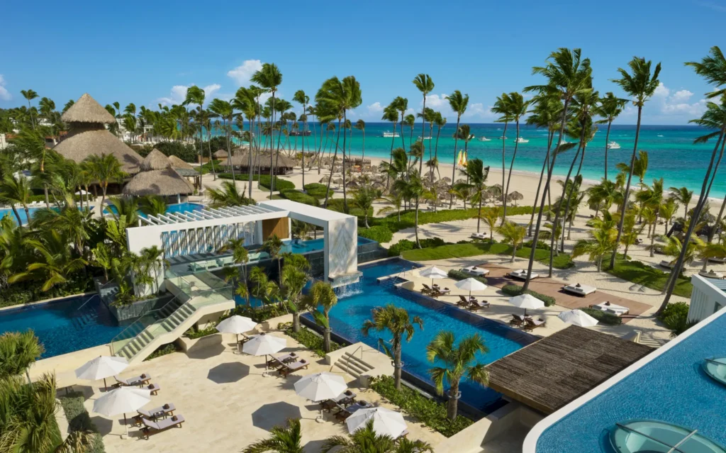 Elevated view of pool decks and beachfront at Secrets Royal Beach Punta Cana with palm trees and sun loungers.