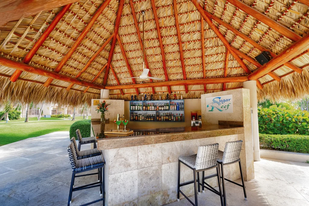 Sugar Reef Plaza Bar at Secrets Royal Beach Punta Cana featuring a tropical palapa bar with thatched roof near the main pool.