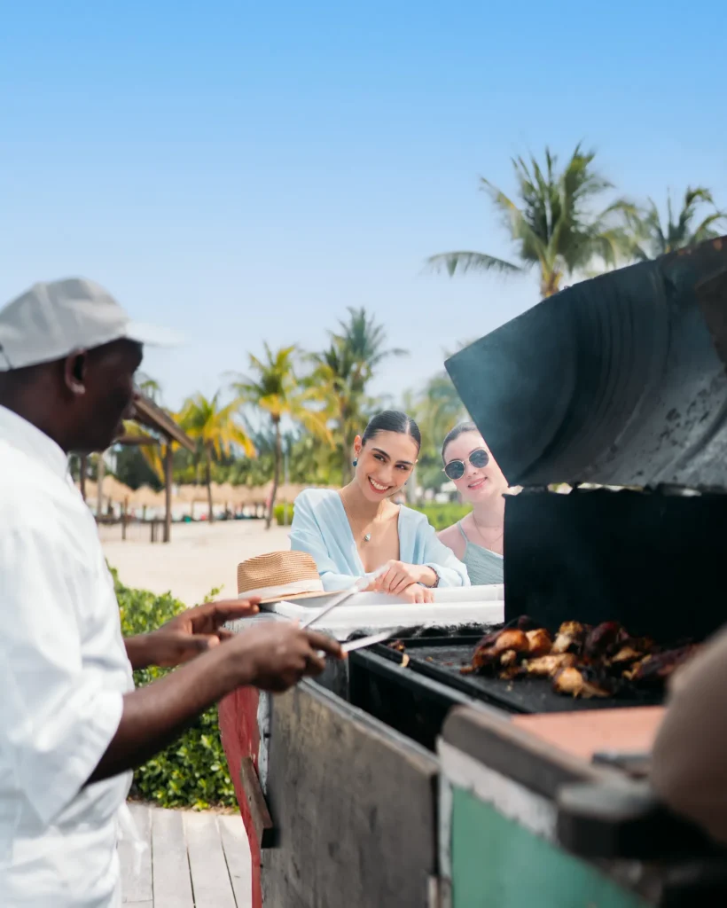 Guests enjoying freshly grilled Jamaican jerk chicken at a beachside grill at Secrets St. James Montego Bay.