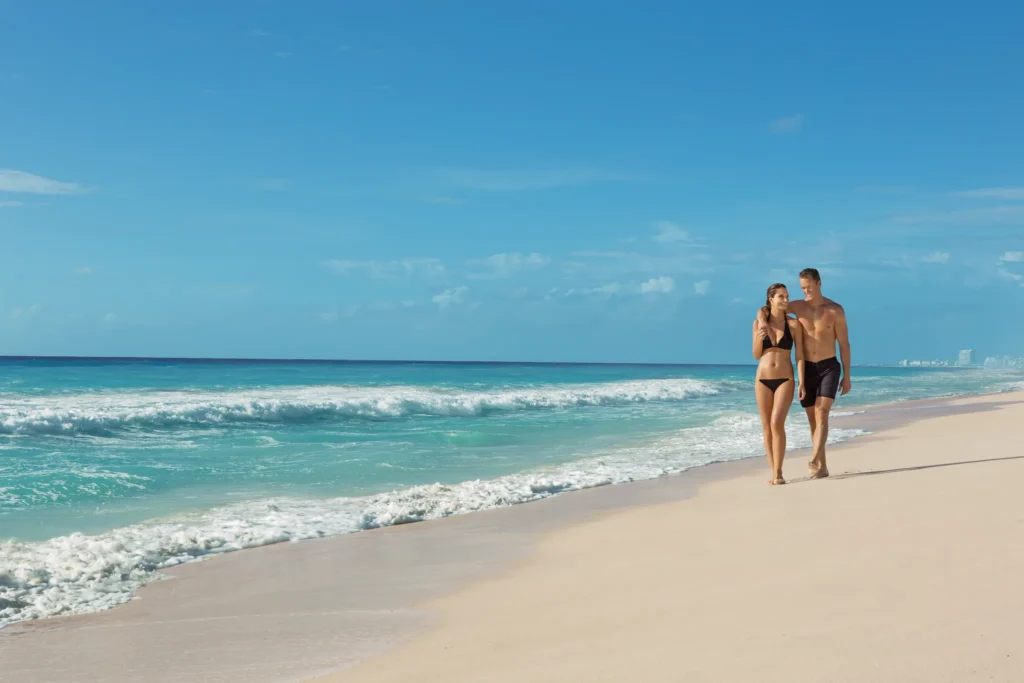 Couple enjoying a peaceful walk along the white sand beach at Secrets The Vine Cancun with turquoise water.
