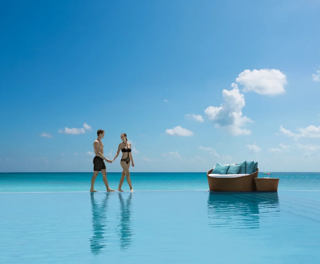 Couple walking hand in hand through an infinity pool overlooking the Caribbean Sea at Secrets The Vine Cancun, perfect for a romantic adults-only getaway.