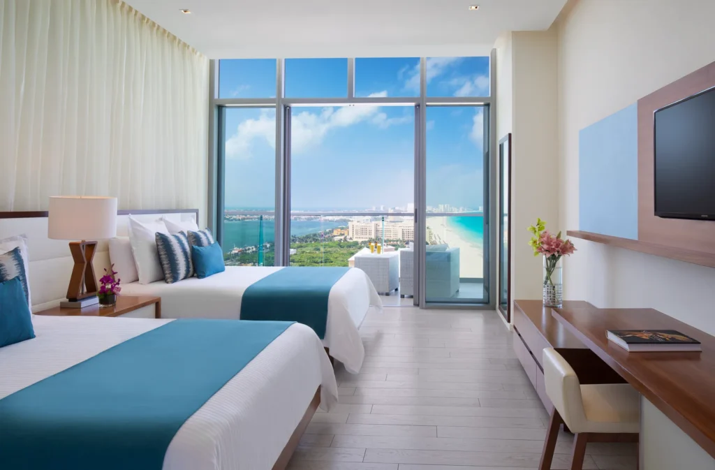 Deluxe Partial Ocean View room with two queen beds and balcony at Secrets The Vine Cancun overlooking the ocean.