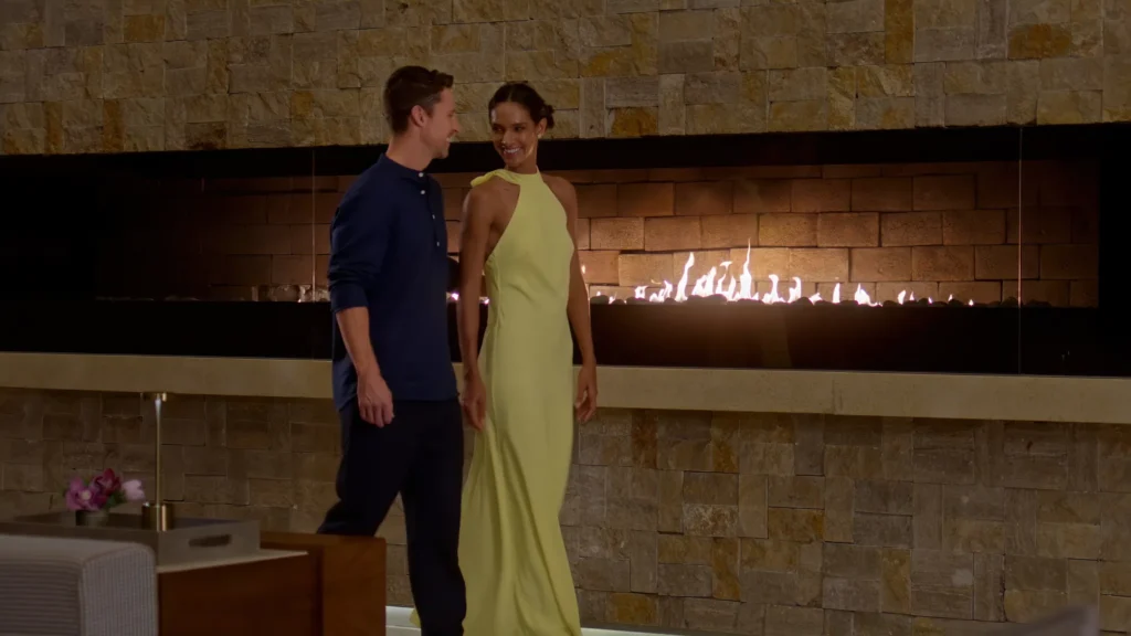 Stylish couple walking past a modern fireplace inside Secrets The Vine Cancun at night.