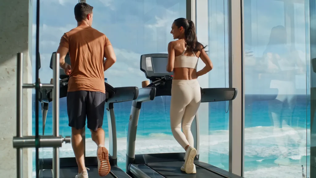 Couple jogging on treadmills overlooking the Caribbean Sea in the fitness center at Secrets The Vine Cancun.