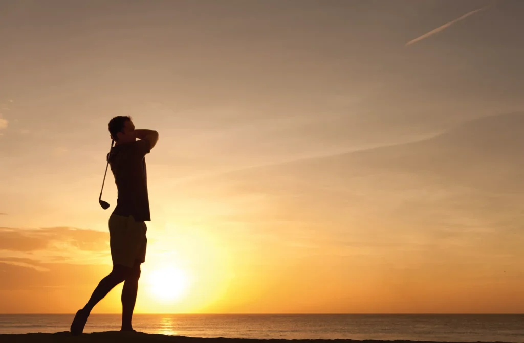Golfer swinging at sunset near Secrets The Vine Cancun with ocean views in the background.