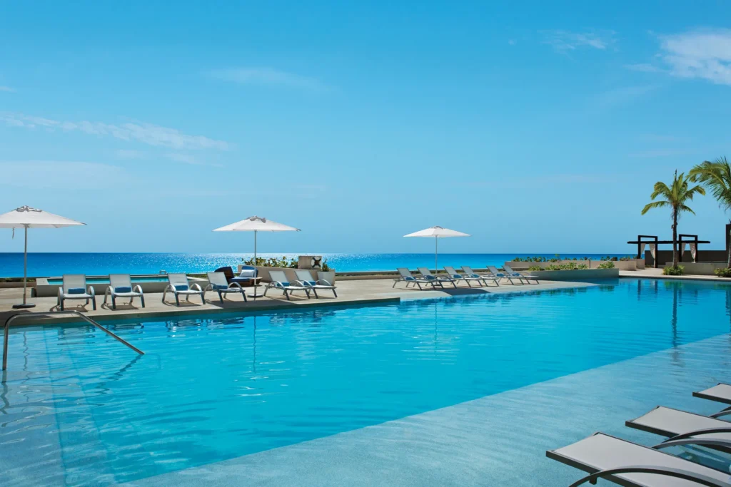 Serene infinity pool with white umbrellas and ocean views at Secrets The Vine Cancun in Cancun’s Hotel Zone.