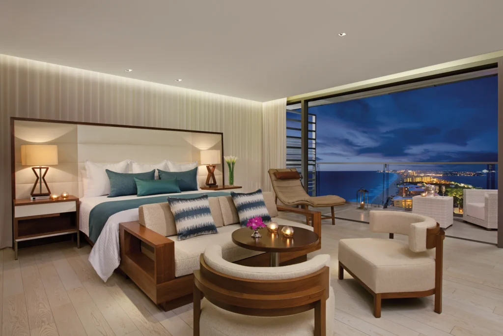 Junior Suite Ocean View at night with king bed and illuminated balcony overlooking Cancun coastline at Secrets The Vine.
