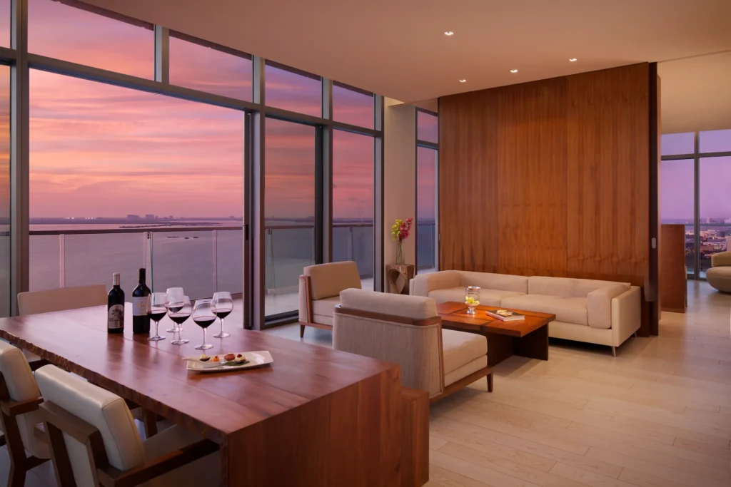 Preferred Club Master Suite Ocean View living area with dining table, sofa, and ocean view at sunset at Secrets The Vine Cancun.