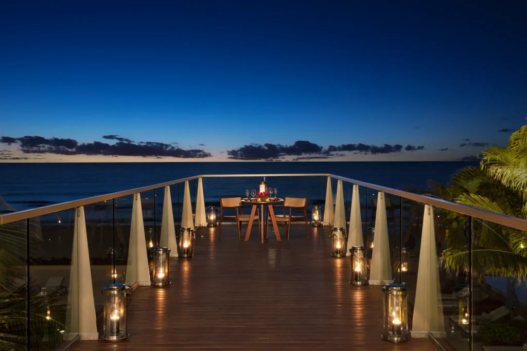 Romantic candlelit dinner setup on a private oceanfront terrace at Secrets The Vine Cancun at sunset.