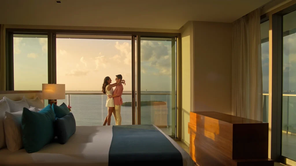 Couple embracing on a private balcony with ocean views at sunset in a suite at Secrets The Vine Cancun.