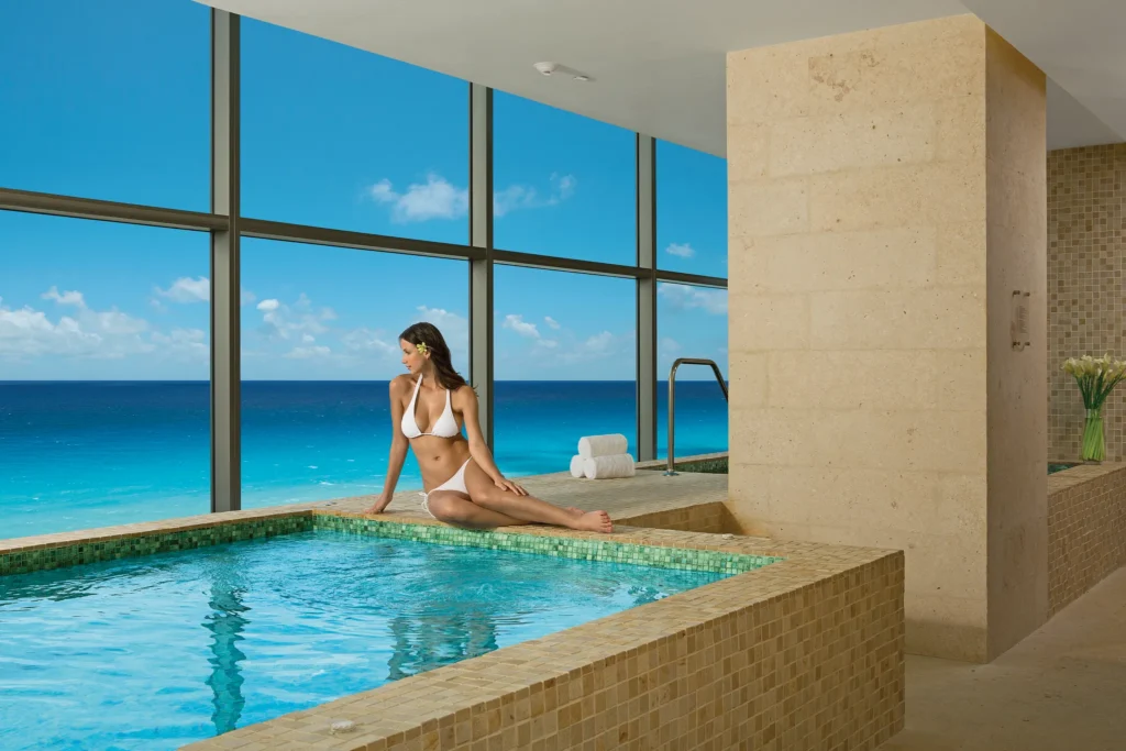 Woman relaxing by an indoor spa whirlpool with ocean views at Secrets The Vine Cancun.