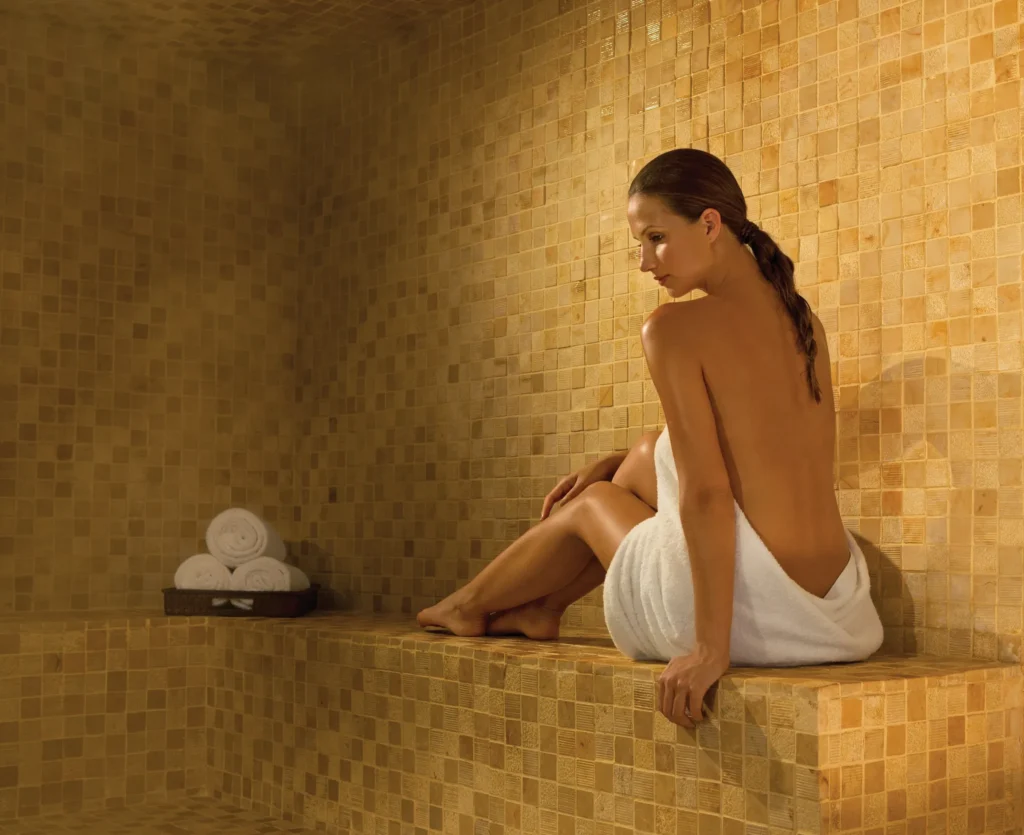 Woman relaxing in a steam room wrapped in a towel at Secrets The Vine Cancun spa.
