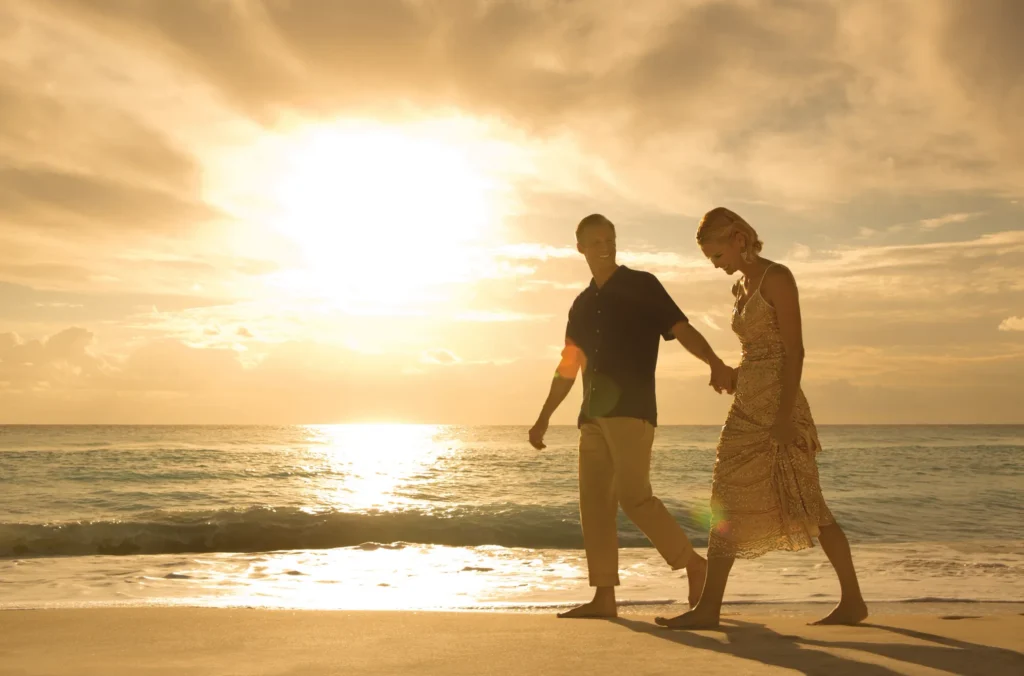 Couple walking along the beach at sunset near Secrets The Vine Cancun with waves and golden sky.