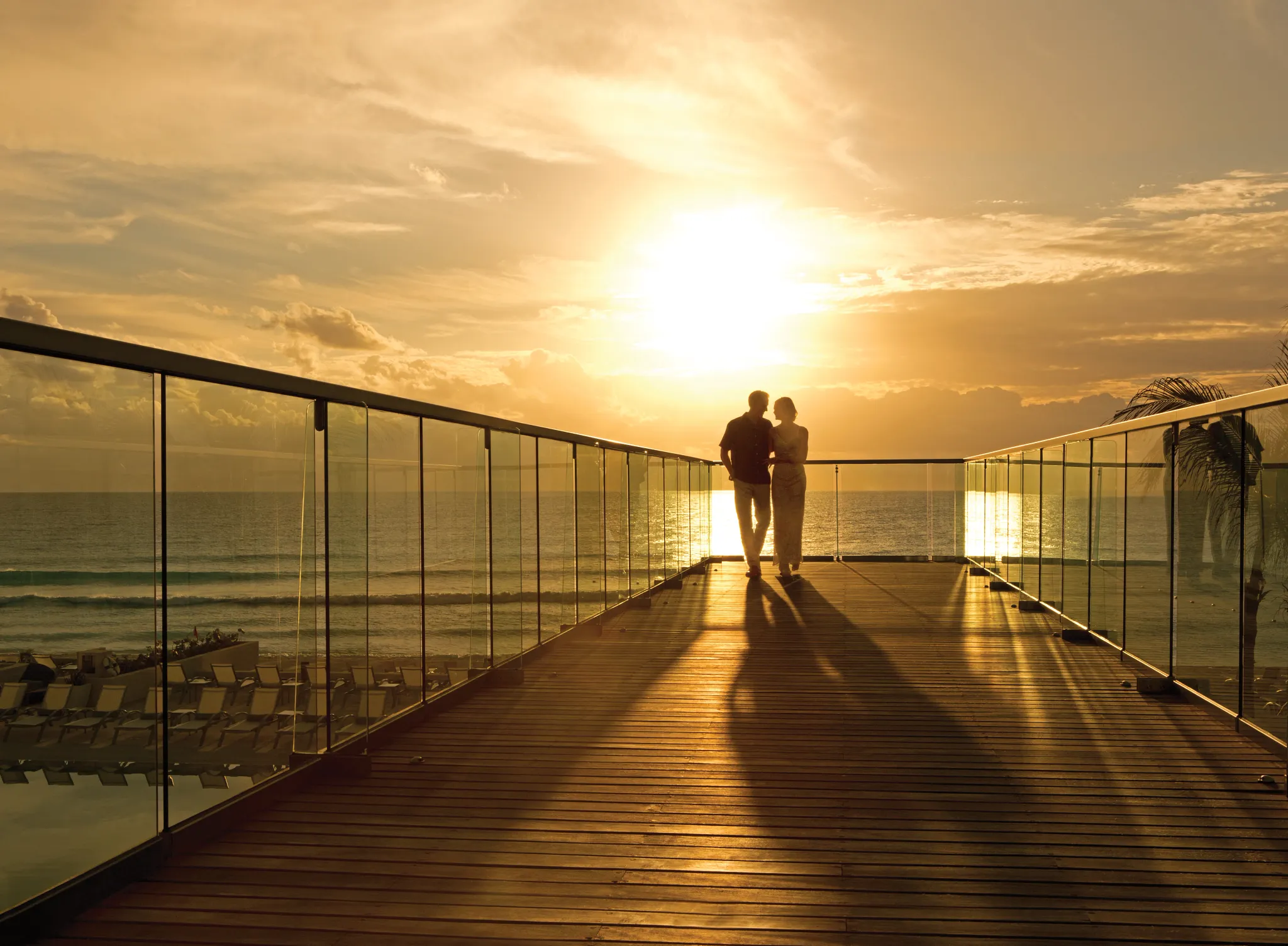 Couple walking on an elevated terrace at sunset overlooking the ocean at Secrets The Vine Cancun.
