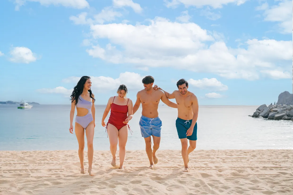 Group of friends walking along the sandy beach at Breathless Cabo San Lucas on a sunny day.