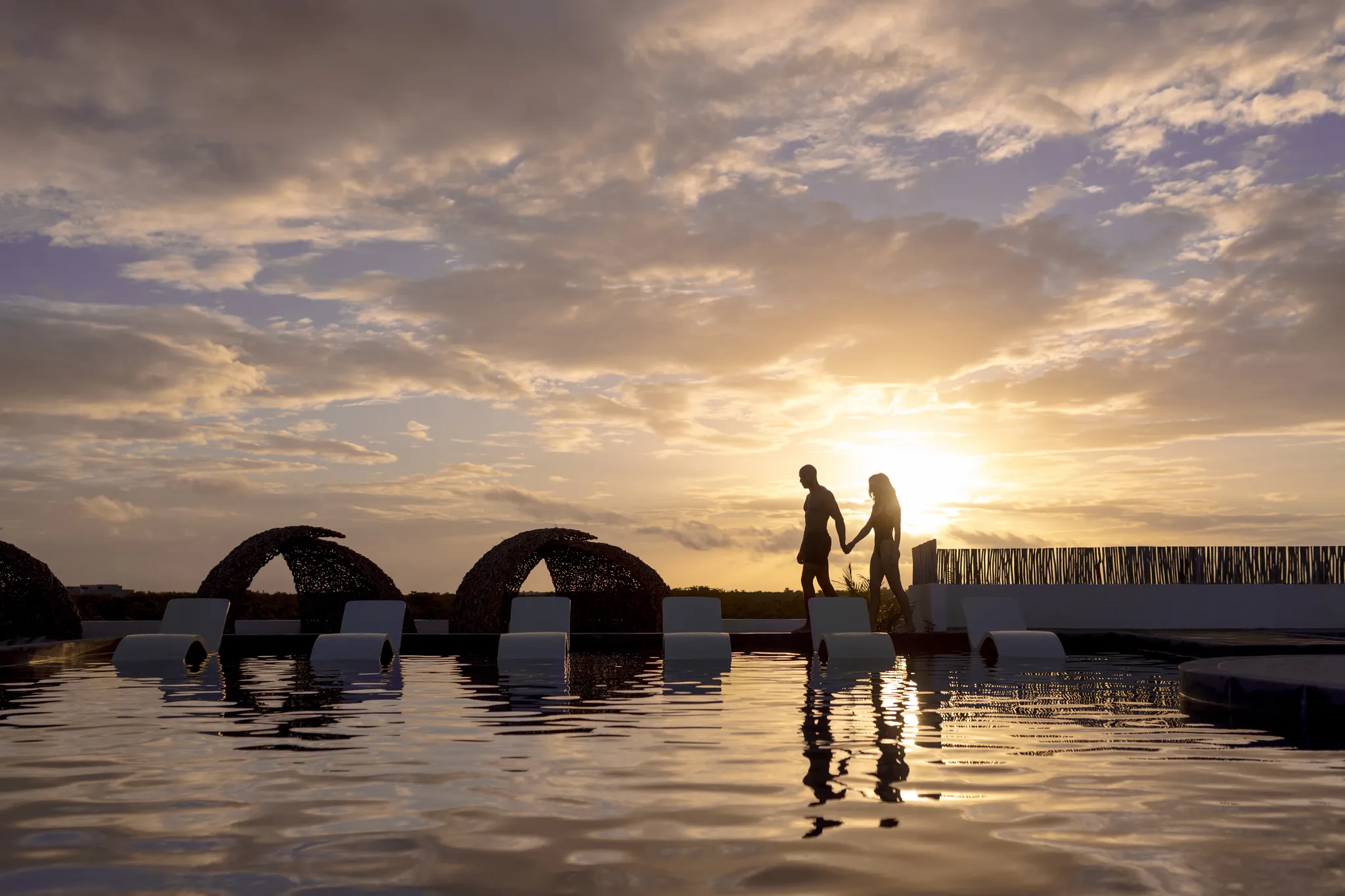 Couple walking beside the rooftop pool at sunset at Secrets Tulum Resort & Beach Club.