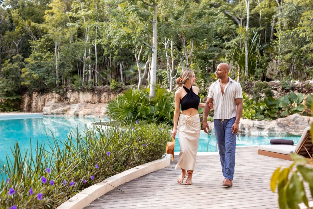 Couple walking along the lagoon-style pool surrounded by lush tropical gardens at Secrets Tulum Resort & Beach Club.