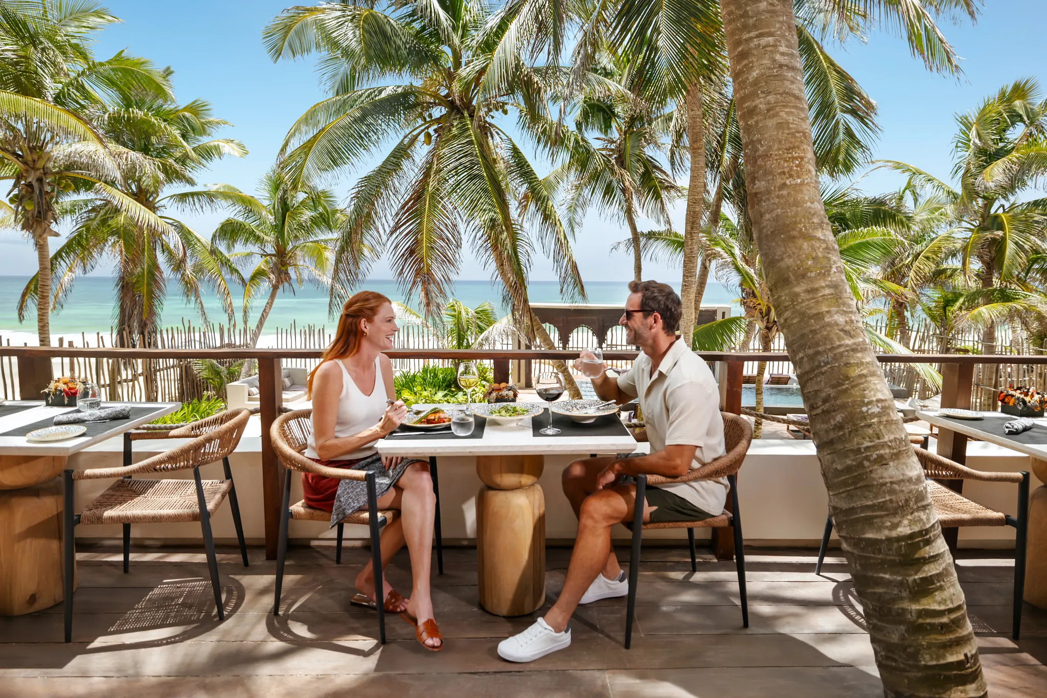 Couple enjoying oceanfront dining surrounded by palm trees at Secrets Tulum Resort & Beach Club.