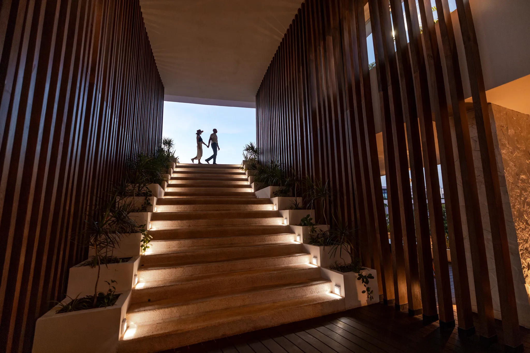 Couple walking up the illuminated staircase inside Secrets Tulum Resort & Beach Club's contemporary lobby.