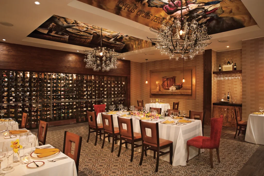 Elegant dining room and wine cellar at Bordeaux restaurant at Secrets Vallarta Bay Puerto Vallarta featuring chandeliers, fine table settings, and extensive wine collection.