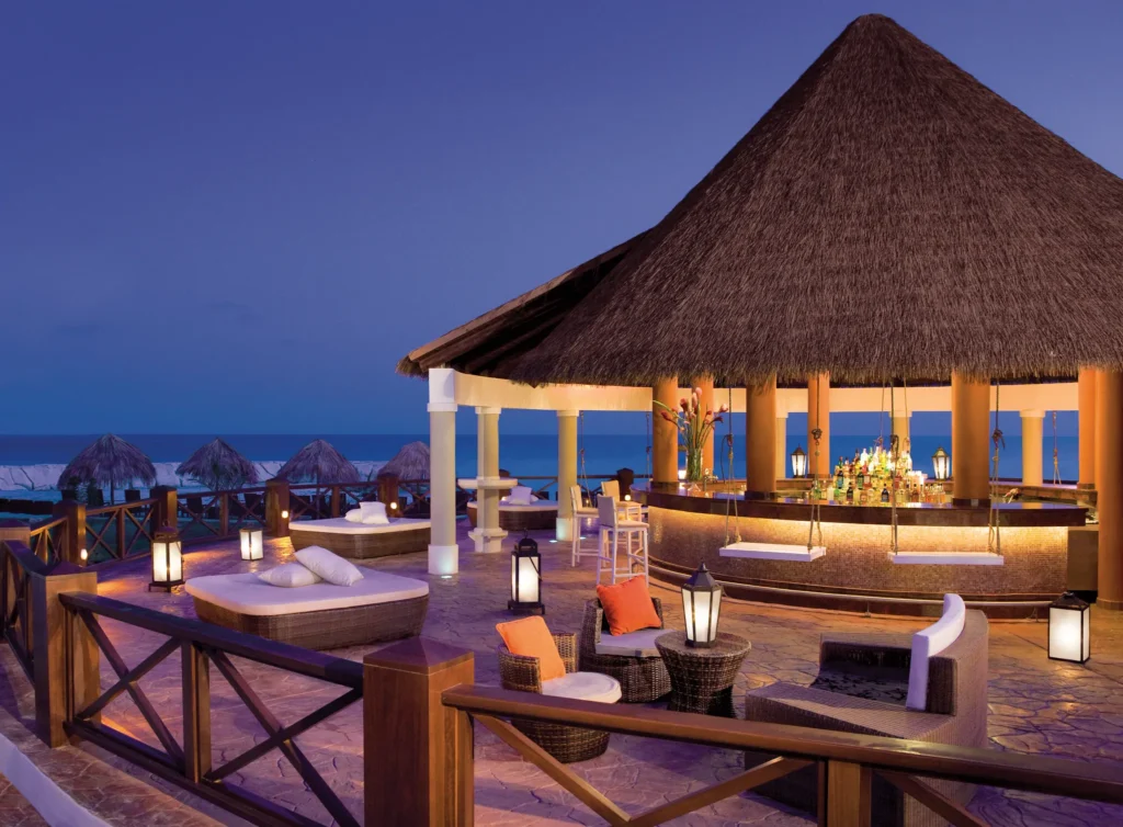Barracuda Beach Bar at Secrets Wild Orchid Montego Bay featuring an open-air thatched-roof bar, premium cocktails, and oceanfront views at sunset.