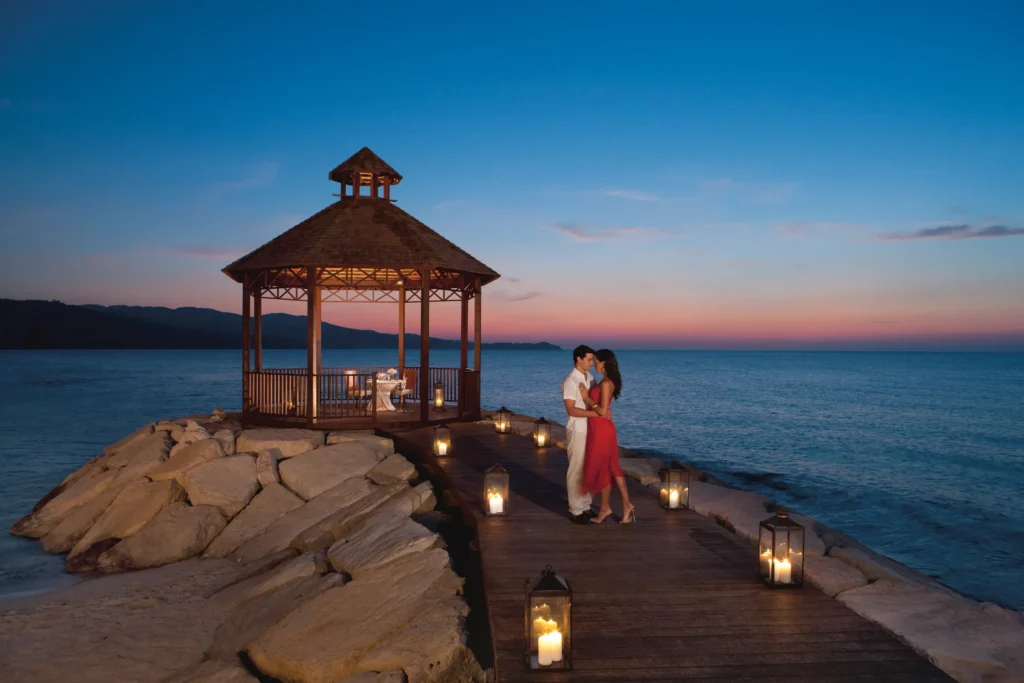Couple enjoying a romantic candlelit dinner at a seaside gazebo at Secrets Wild Orchid Montego Bay at sunset.