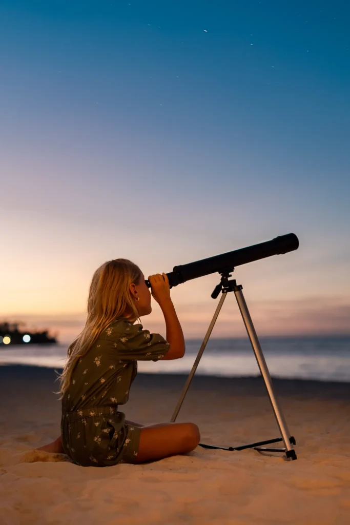 Child using a telescope for stargazing on the beach at sunset at Sunscape Coco Punta Cana Resort.
