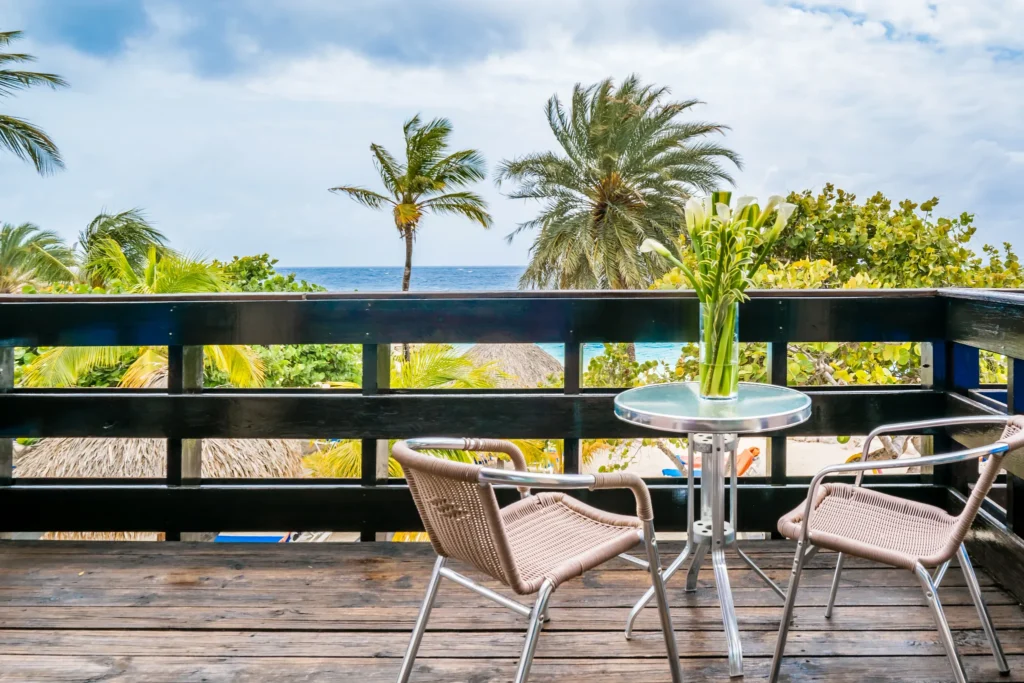 Private oceanfront balcony with seating and palm tree views at Sun Club Premium Deluxe Ocean Front room at Sunscape Curaçao Resort.