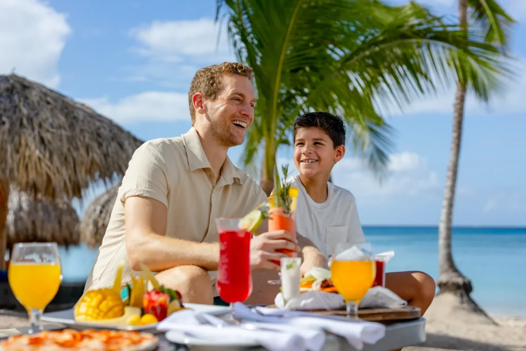 Father and son enjoying lunch with tropical drinks by the beach at Sunscape Dominicus La Romana.