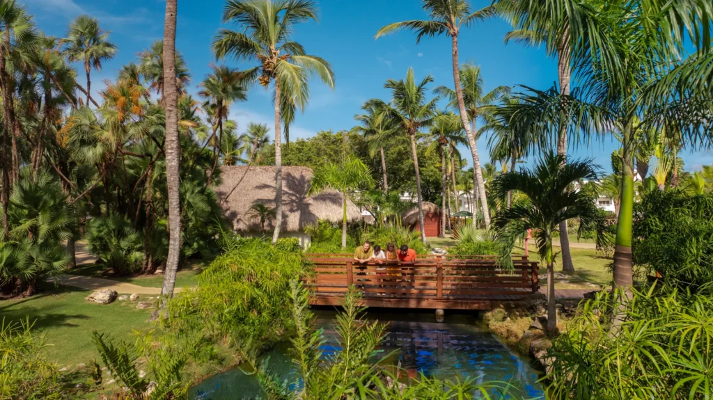 Family exploring a wooden bridge over a tropical garden lagoon at Sunscape Dominicus La Romana.