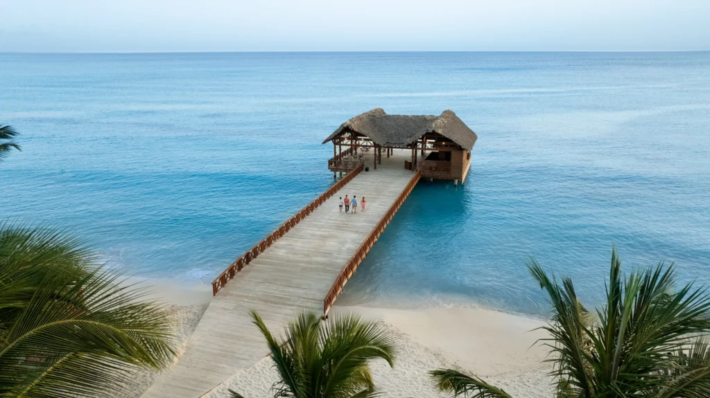 Family walking along a wooden pier toward an overwater palapa at Sunscape Dominicus La Romana in the Dominican Republic.
