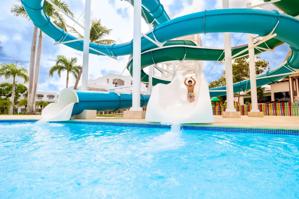 Child sliding down a large water slide into a pool at Sunscape Dominicus La Romana waterpark.