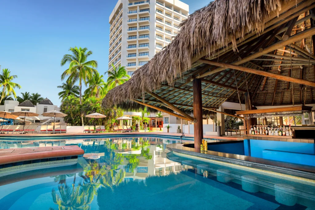 Manatees Swim-Up Bar at Sunscape Dorado Pacifico Ixtapa featuring a thatched-roof pool bar, in-water seating, and tropical resort surroundings.