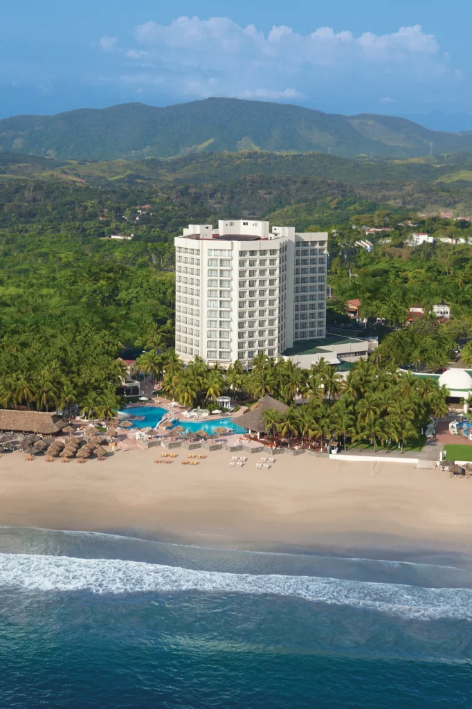 Aerial view of Sunscape Dorado Pacifico Ixtapa, a beachfront all-inclusive resort with pools, palm trees, and golden sand along the Pacific Ocean.
