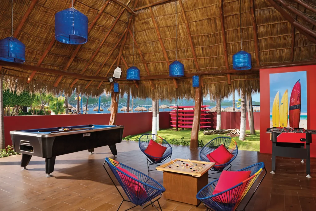 Guests relaxing and playing games in the Core Zone entertainment area at Sunscape Puerto Vallarta Resort & Spa, featuring a palapa lounge with ocean views.