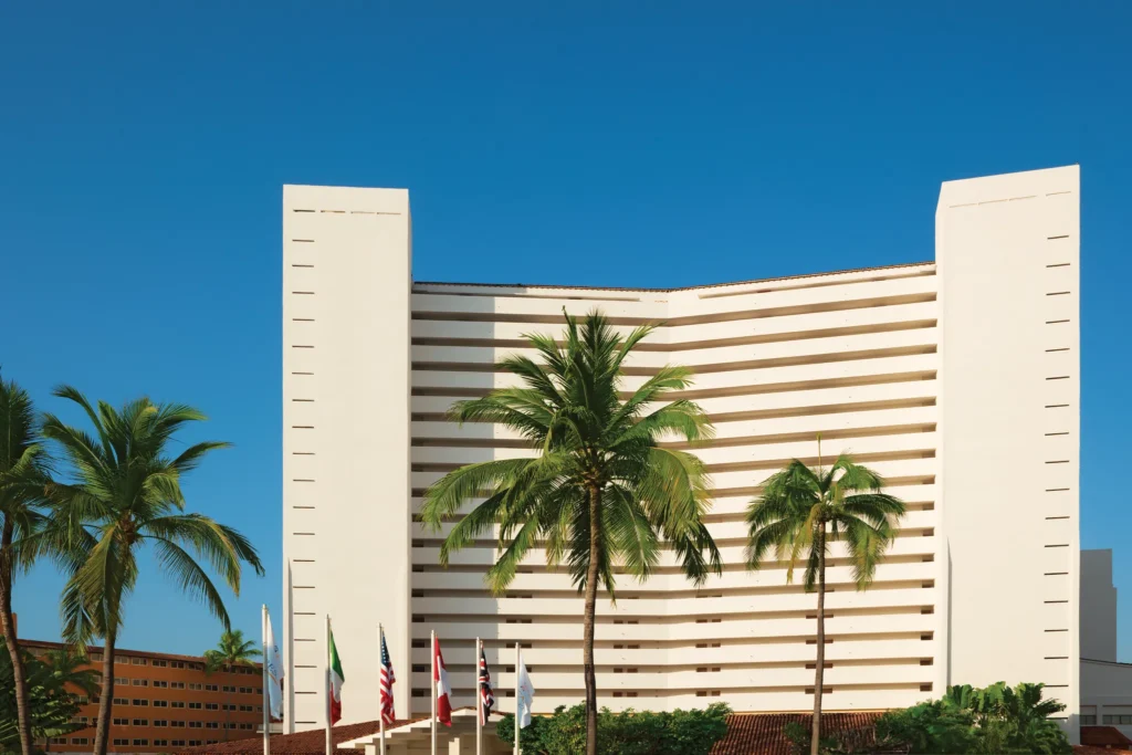 Exterior view of Sunscape Puerto Vallarta Resort & Spa with palm trees and a modern beachfront hotel façade under clear blue skies.