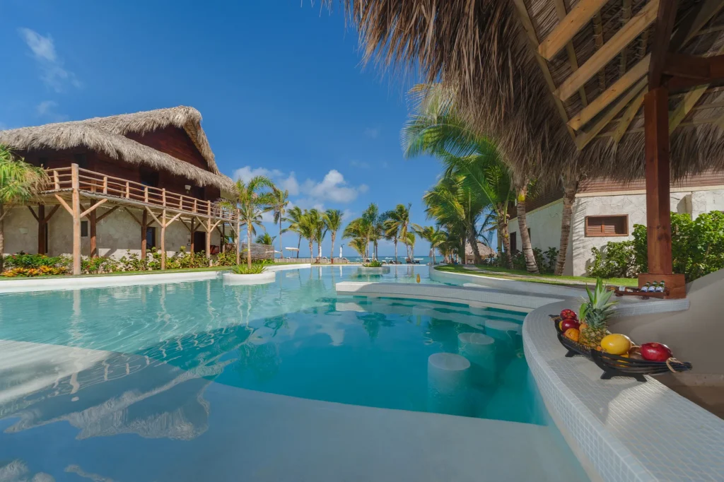 Caicu Swim-Up Bar at Zoëtry Agua Punta Cana featuring a beachfront infinity pool, thatched-roof architecture, and tropical Caribbean setting.