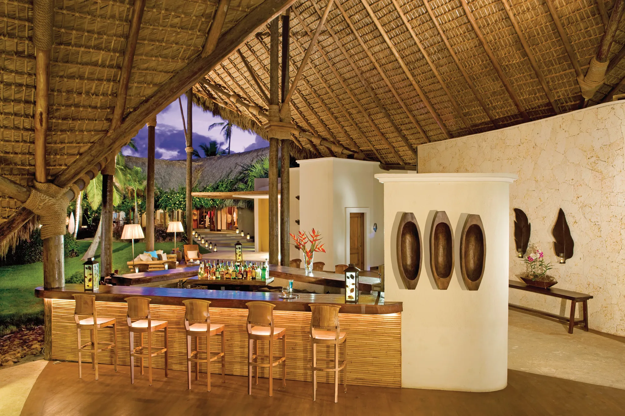 Canoa Lobby Bar at Zoëtry Agua Punta Cana featuring an open-air thatched roof, tropical ambiance, and elegant wooden bar seating.