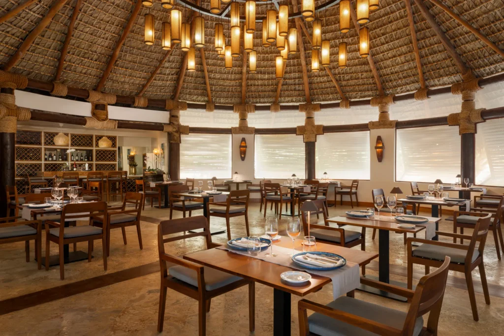 Olena Restaurant at Zoëtry Agua Punta Cana featuring elegant Italian dining, warm wood interiors, and a thatched-roof ceiling with ambient lighting.