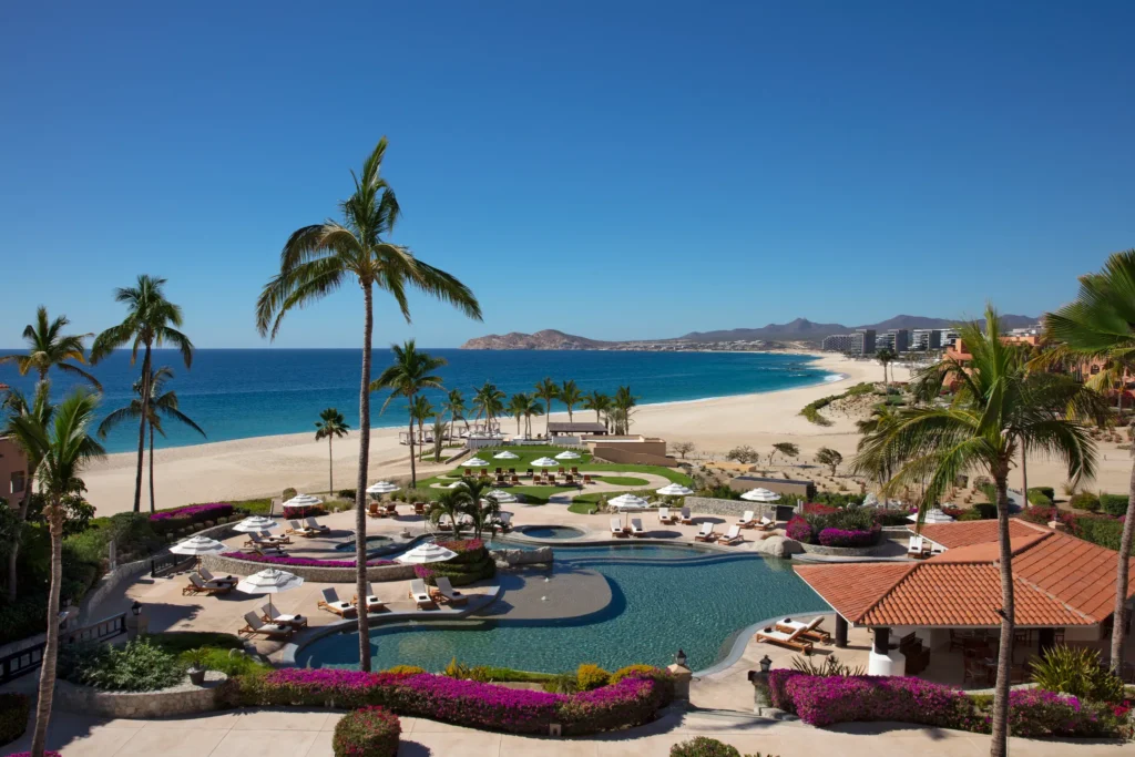 Resort pool overlooking beach and ocean at Zoëtry Casa del Mar Los Cabos with palm trees and lounge chairs.