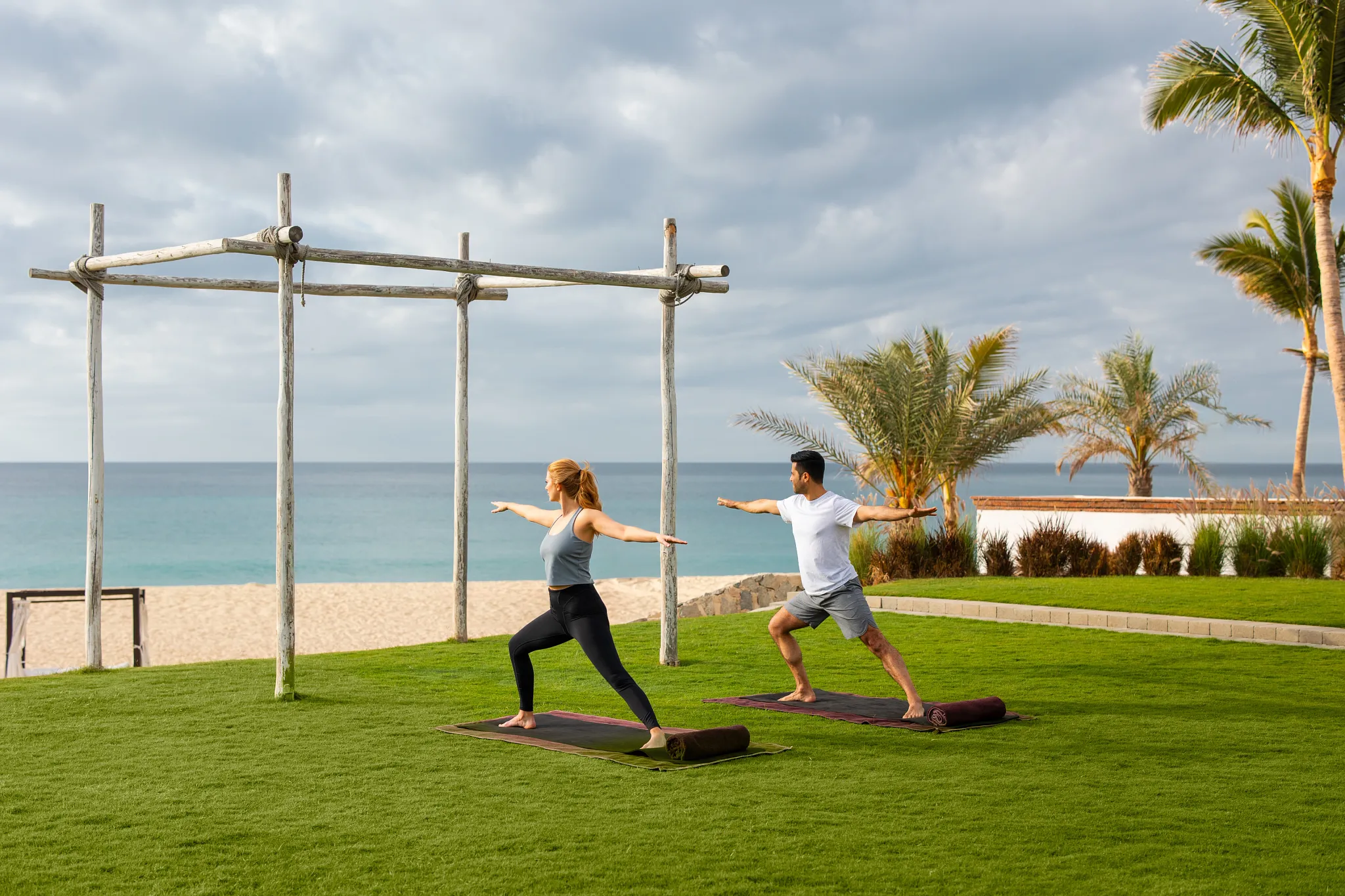 Guests practicing yoga on lawn overlooking beach at Zoëtry Casa del Mar Los Cabos.
