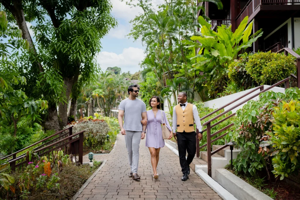 Couple walking with a resort concierge through lush tropical gardens at Zoëtry Marigot Bay St. Lucia.