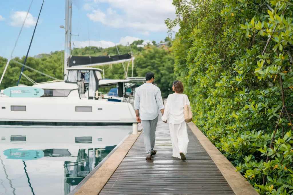 Couple strolling hand-in-hand along the marina boardwalk at Zoëtry Marigot Bay St. Lucia near luxury yachts.