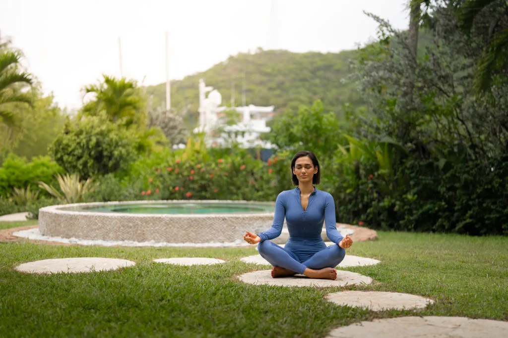Woman meditating in a lush tropical garden at Zoëtry Marigot Bay St. Lucia with marina views in the distance.