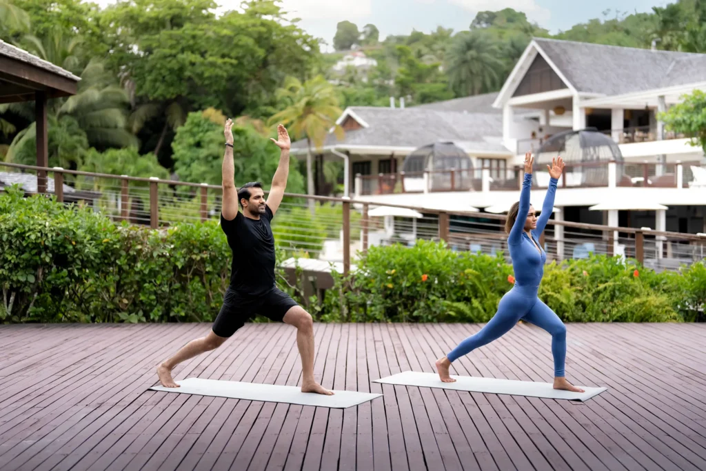 Couple practicing morning yoga on a wooden deck at Zoëtry Marigot Bay St. Lucia surrounded by tropical gardens.