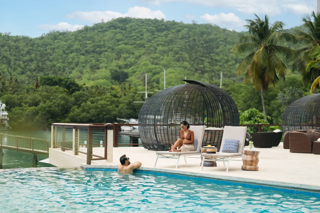 Couple relaxing by the infinity pool at Zoëtry Marigot Bay St. Lucia with lush hillside views.