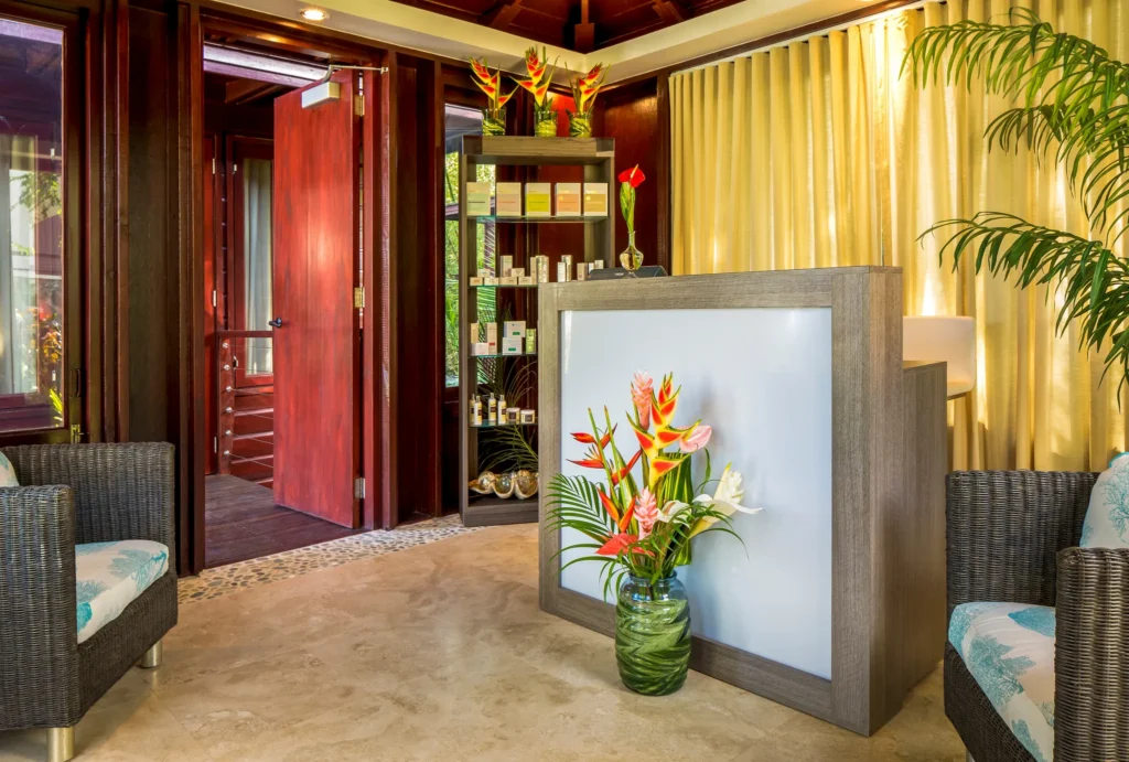 Elegant spa reception desk with tropical flowers and warm wood accents at Zoëtry Marigot Bay St. Lucia.